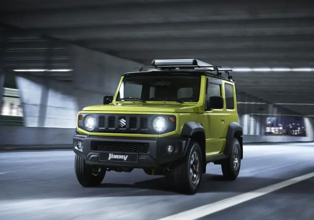 Suzuki Jimny amarillo mostaza conduciendo por una calle urbana.